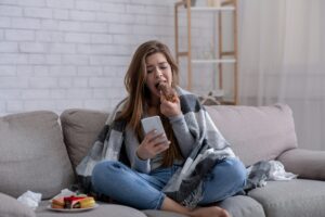 Emotional eating concept. Upset young woman with sweet pastry looking at smartphone, waiting for