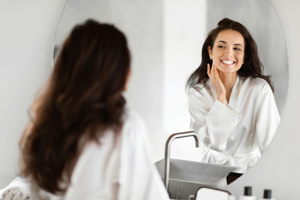 Smiling woman admiring herself in bathroom mirror